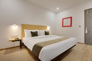 A hotel room with a bed, bedside table, and a framed picture on the wall.