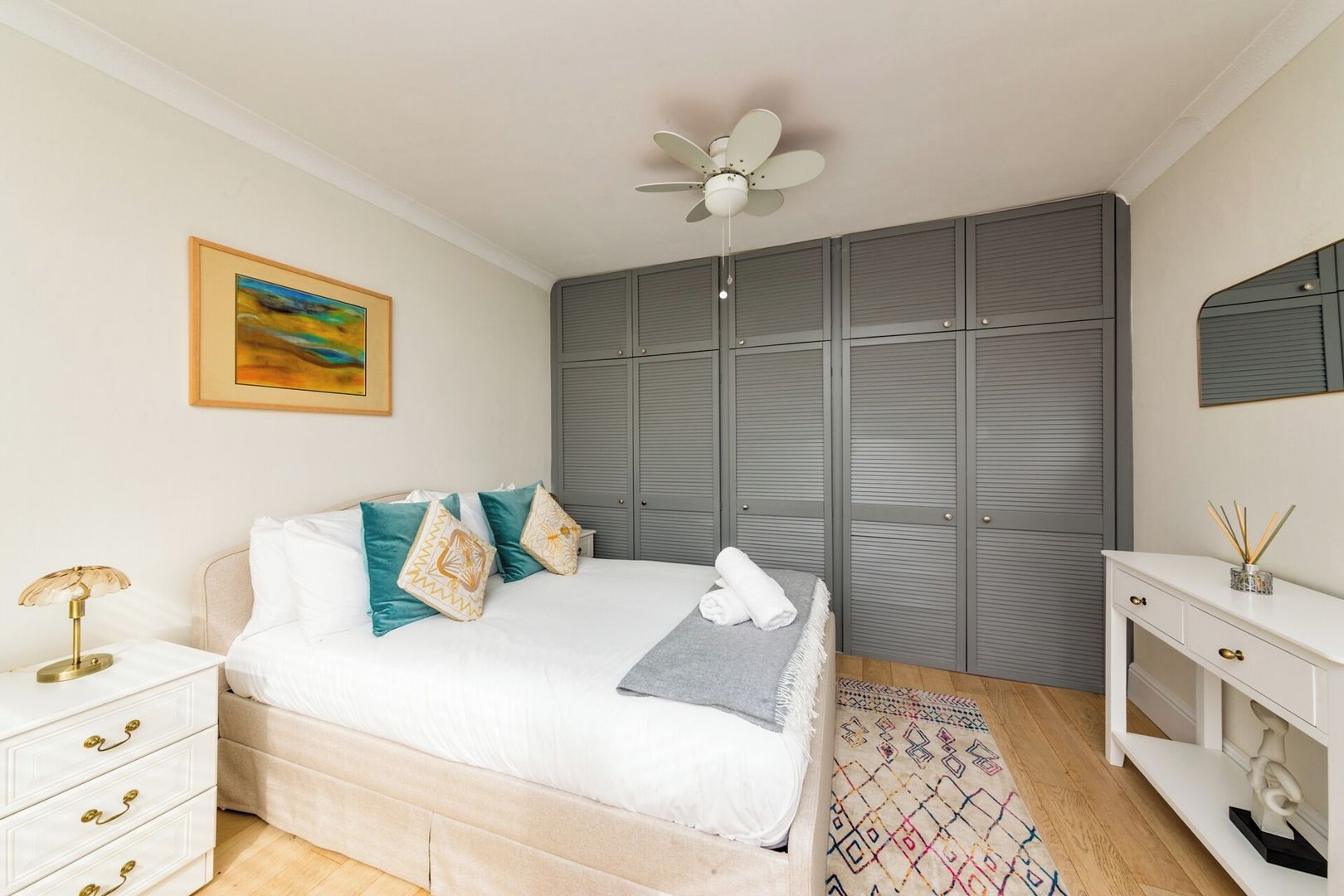 A bedroom with a bed, bedside table, wardrobe, and a ceiling fan.