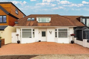 A two-story house with a brick driveway, white exterior, and a small front garden. - Lancing 3BR Home | Parking for 3 Cars (West Sussex)