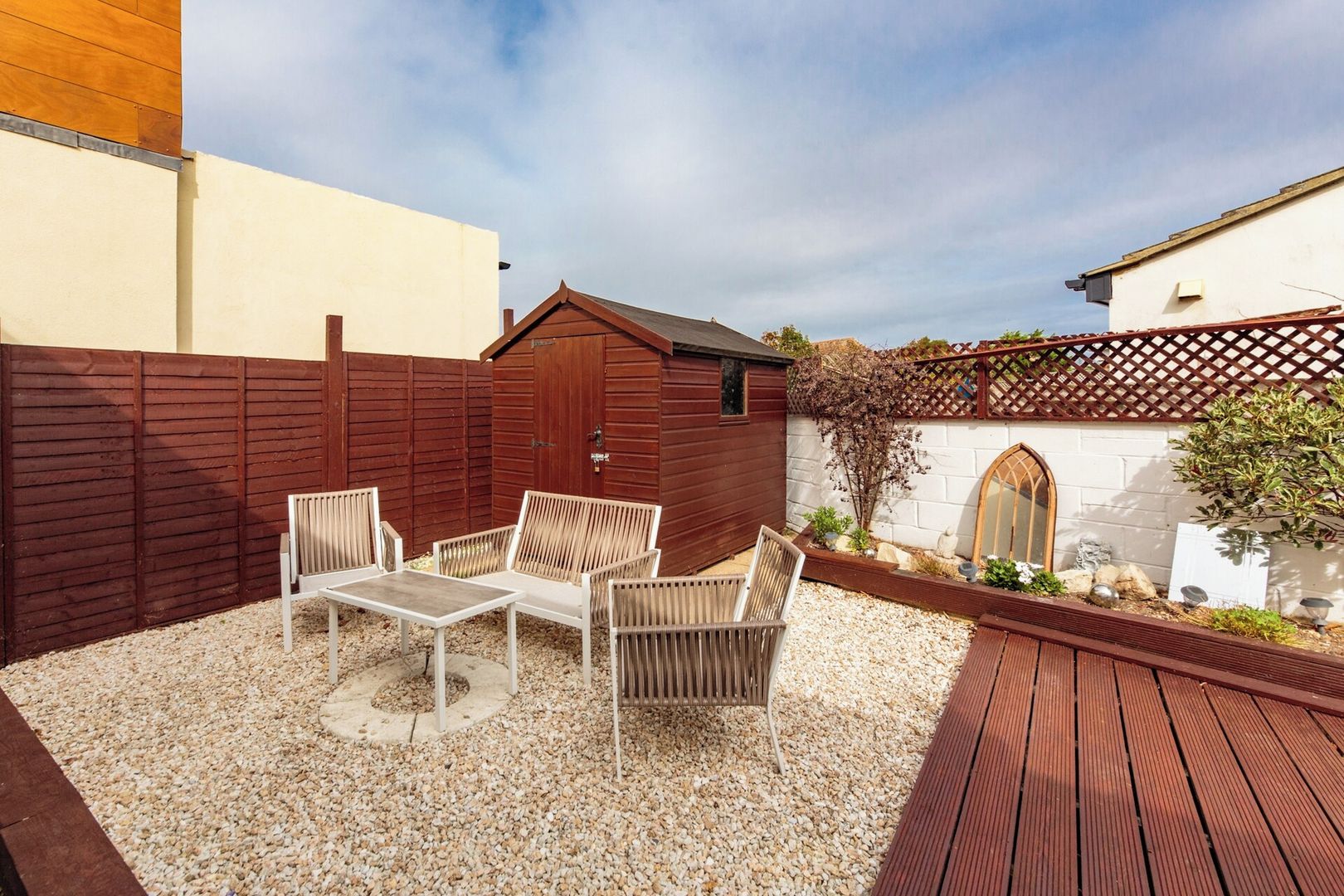 A patio area with a table and chairs, a wooden fence, and a white building with a window.