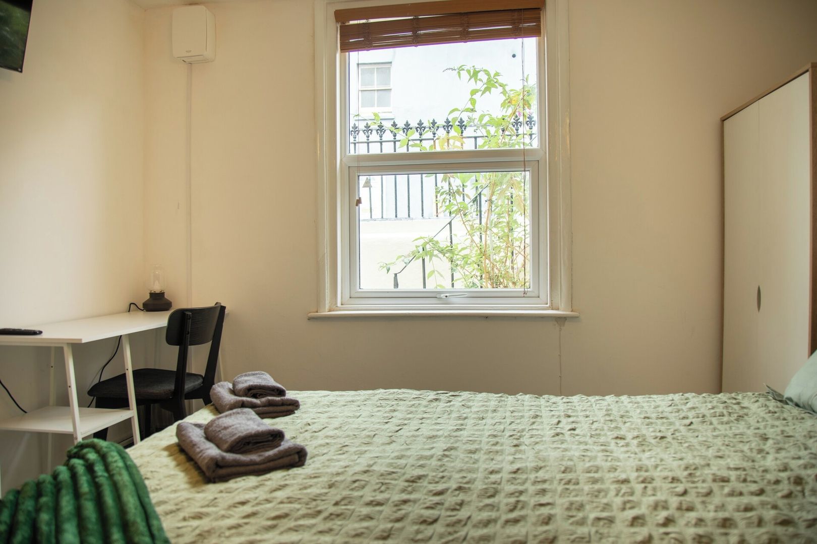 Un dormitorio con cama, escritorio, silla y ventana con vistas a zonas verdes.
