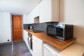 A kitchen with white cabinets, a wooden countertop, a microwave, a stove, and a dishwasher. - Cosy 1-Bed Garden Flat by Brighton Station (Brighton and Hove)