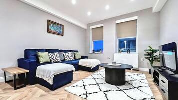 A modern living room with a blue sofa, a round coffee table, and a white rug.