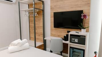 Una habitación de hotel con cama, escritorio con televisor, un refrigerador pequeño y vestidor.