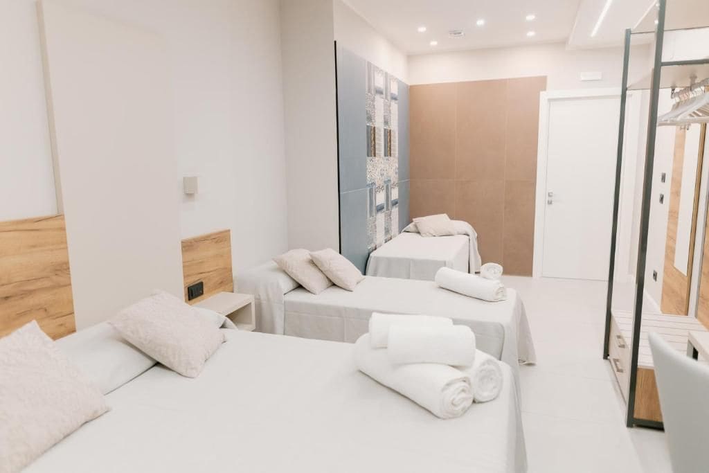 Habitación de hotel con dos camas, cabecera de madera, una obra de arte en la pared y mampara de ducha de vidrio.