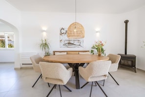 A dining area with a round wooden table, six chairs, a hanging light fixture, a wall-mounted fish illustration, and a wood-burning stove. - Luxury Lagos Villa, with Seaview. Close to the Old Town and pristine beaches (Lagos)