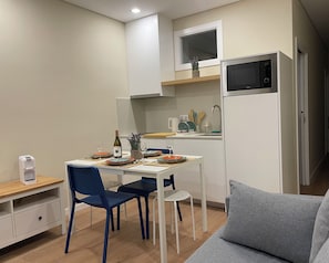 Een kleine keuken met een magnetron, een spoelbak en een eethoek, gedekt met borden, glazen en een fles.