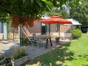 Eine Terrasse mit Tisch und Stühlen, eine Backsteinmauer und ein überdachter Sitzbereich.
