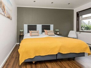 Ein modernes Schlafzimmer mit einem Doppelbett, einer gelben Tagesdecke und Blick ins Freie durch ein Fenster.