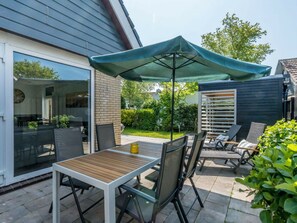 Eine Terrasse im Freien mit Tisch und Stühlen, einem schattenspendenden Sonnenschirm und einem Holenzaun.