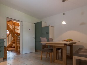 Ein Essbereich mit einem Holztisch und Stühlen, einer Leuchte darüber und einer Treppe, die zu einem anderen Raum führt.