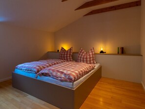 Ein Schlafzimmer mit einem Bett, karierten Bettwäsche, einem Nachttisch mit einer Lampe und Holzbalken an der Decke.