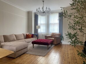 A living room with a beige sofa, a red ottoman, a wooden coffee table, a chandelier, and a plant. - Spacious 5-Bed Victorian Home with Garden near Richmond & London (Richmond)