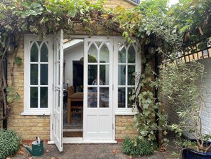 A house with a white door and windows, a brick wall, and a garden with plants and a watering can. - Spacious 5-Bed Victorian Home with Garden near Richmond & London (Richmond)