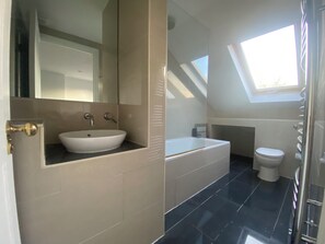 A modern bathroom with a white sink, a bathtub, and a toilet. There is a skylight above the toilet. - Spacious 5-Bed Victorian Home with Garden near Richmond & London (Richmond)