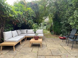 Une terrasse de jardin avec une table en bois, un canapé gris et un fauteuil noir.