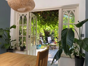 A dining area with a wooden table and chairs, a wicker pendant light, and a view of a lush garden through a white-framed glass door. - Spacious 5-Bed Victorian Home with Garden near Richmond & London (Richmond)