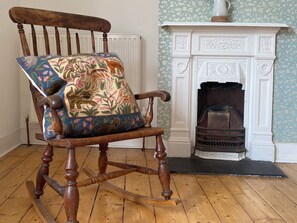 Un fauteuil à bascule en bois avec un coussin à motifs floraux, dans une pièce dotée d’une cheminée.