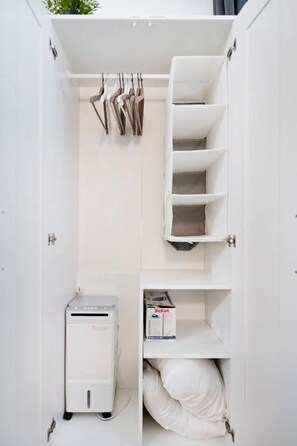 Ein weißer Kleiderschrank mit Kleiderstange, Regalen und Platz für ein kleines Gerät.