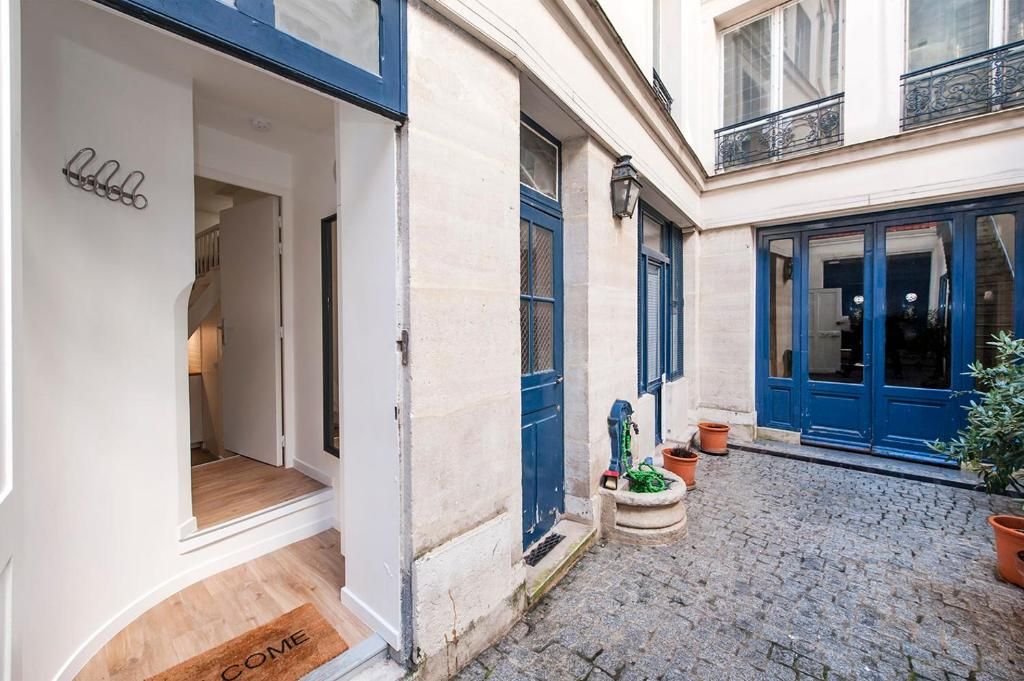 A courtyard with a cobblestone path, a door with a 'welcome' mat, and a potted plant.