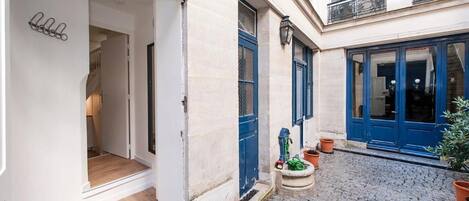 A courtyard with a cobblestone path, a door with a 'welcome' mat, and a potted plant.