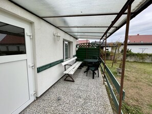 Ein überdachter Patio-Bereich mit einer Bank, einem Tisch und Stühlen.