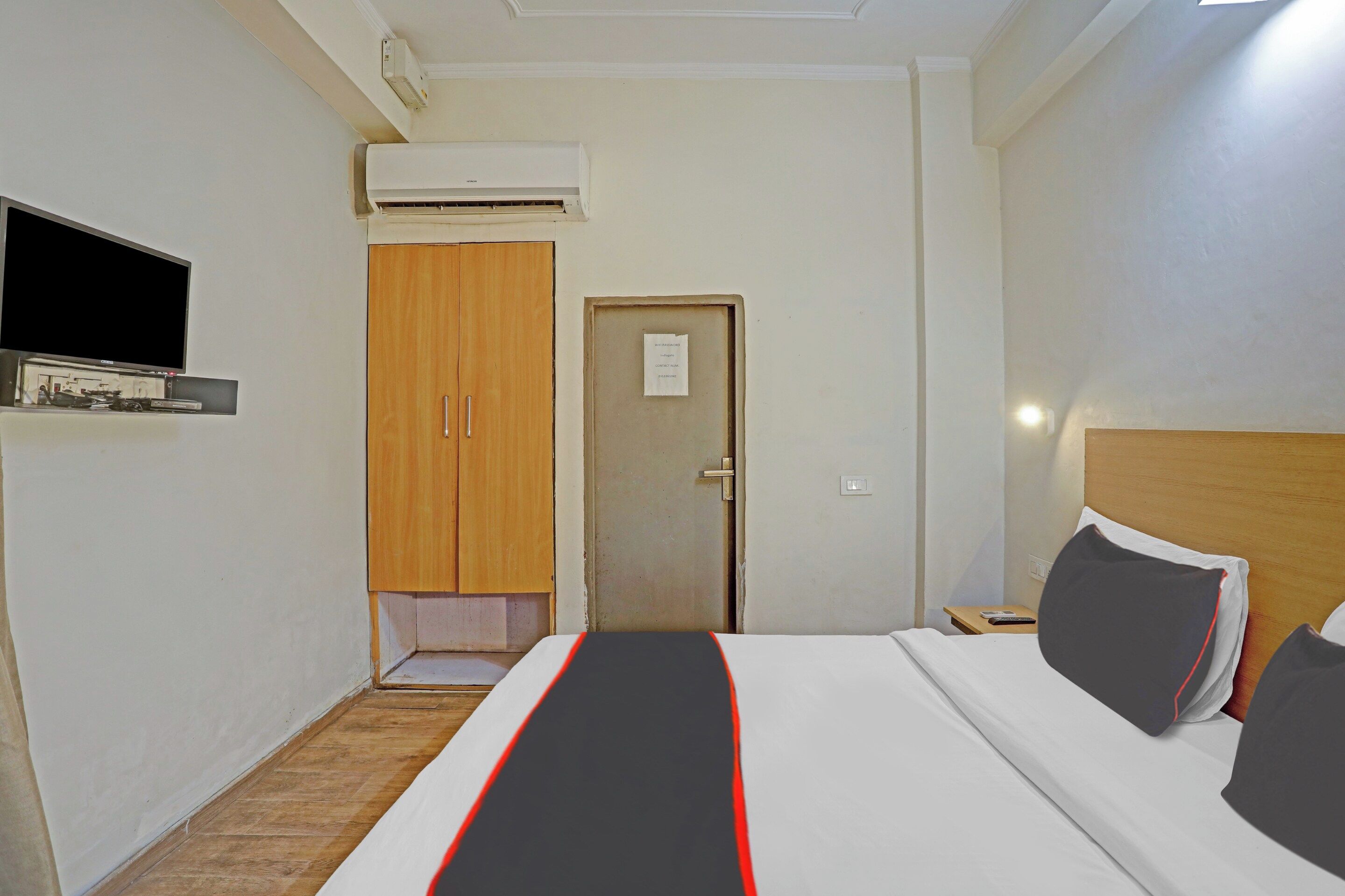 Ett hotellrum med en säng, en tv, en luftkonditioneringsanläggning och en garderob i trä.