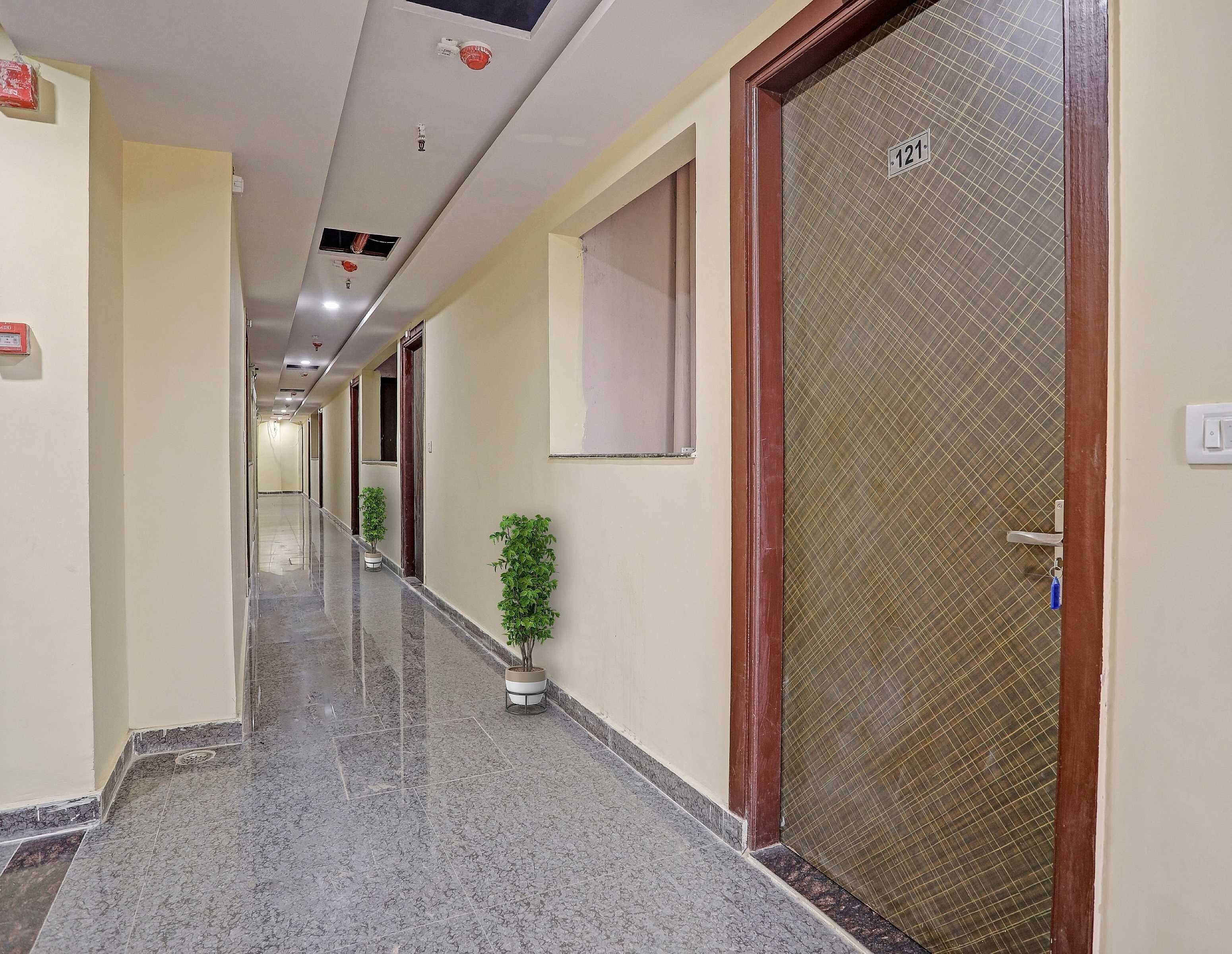 Un pasillo de hotel con piso de mármol, plantas en macetas y una puerta con placa de número.