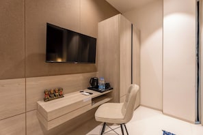 Una habitación de hotel moderna con una televisión de pantalla plana montada en la pared, un tocador de madera con espejo, una pequeña zona de estar con una silla y una cafetera en la encimera.
