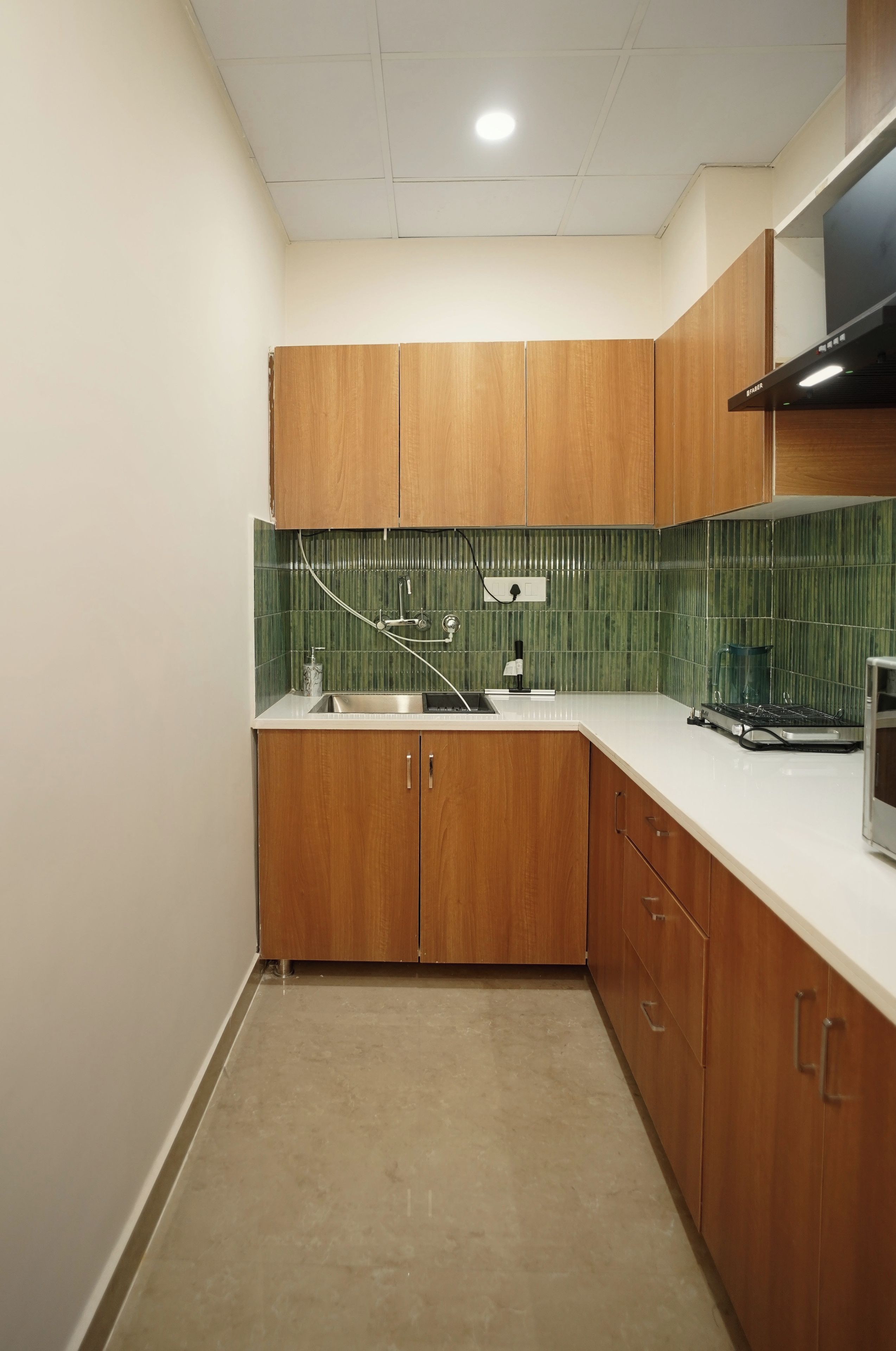 A compact kitchen with wooden cabinets, a stainless steel sink, and a green tiled backsplash.