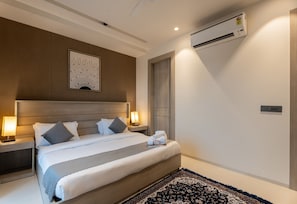 A hotel room with a bed, nightstands, a wall-mounted air conditioner, and a decorative piece above the bed. - The Lodgers Vertex 1 BHK Apartments (Gurugram)