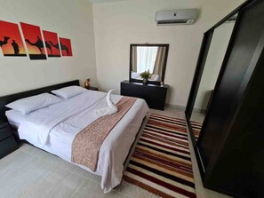 A hotel room with a bed, a bedside table, a mirror, and a wall-mounted air conditioner. - Sunshine & Smiles Nabqs Most Lovely Apartment (Sharm El Sheikh)