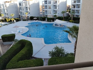 A swimming pool surrounded by well-maintained hedges and palm trees, with a view of residential buildings in the background. - Sunshine & Smiles Nabqs Most Lovely Apartment (Sharm El Sheikh)