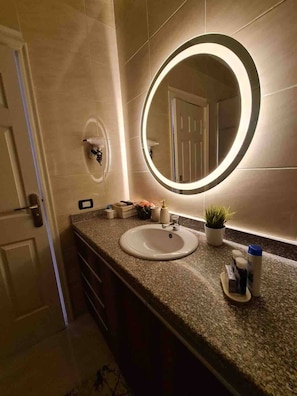 A bathroom with a round mirror, a sink, and a potted plant. - Sunshine & Smiles Nabqs Most Lovely Apartment (Sharm El Sheikh)