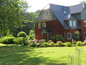 A two-story house with a balcony, surrounded by a well-maintained garden with various plants and flowers. - Holiday Apartment With 2 Bedrooms (Heringsdorf)