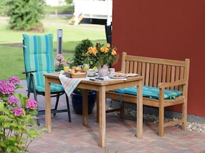 An outdoor seating area with a wooden table, chairs, and a bench. There is a potted plant with flowers on the table. - Holiday Apartment With 2 Bedrooms (Heringsdorf)