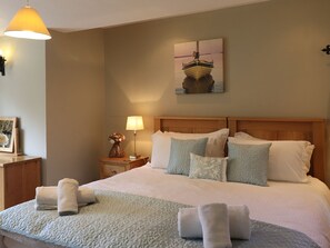 A hotel room with a large bed, a nightstand with a lamp, a framed picture on the wall, and a painting above the bed. - Highbeck (Kendal)