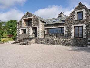 A stone house with a sloped roof, a balcony, and a fenced driveway. - Highbeck (Kendal)