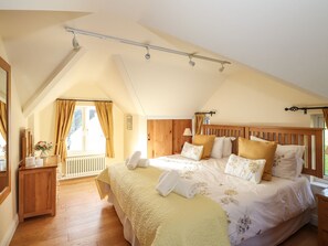Ein Schlafzimmer mit schrägen Wänden, einem hölzernen Bettgestell, einem Nachttisch und einem Fenster mit Vorhängen.