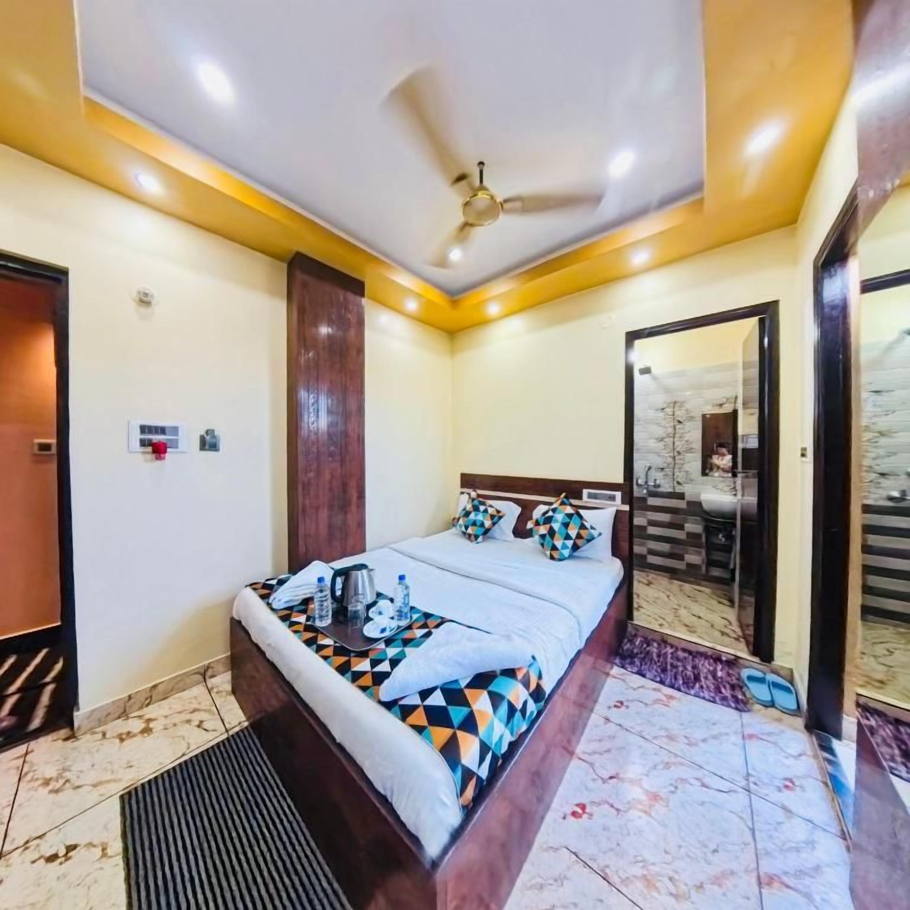 Una habitación de hotel con una cama, ventilador de techo, baño con espejo y suelo de baldosas.
