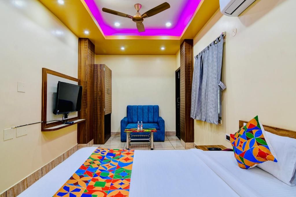 Una habitación de hotel con cama, televisor, ventilador de techo, sofá azul y alfombra colorida.