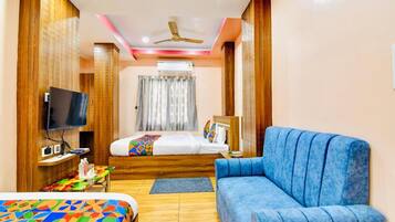 A hotel room with a bed, a blue sofa, a television, and a ceiling fan.