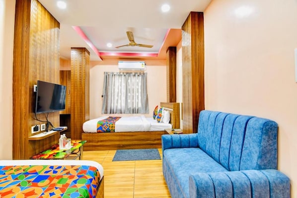 A hotel room with a bed, a blue sofa, a television, and a ceiling fan. - Hotel Kanan Inn - Kolkata Airport (Barakpur)