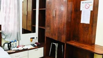 A hotel room with a large wardrobe, a bed with a patterned bedspread, a desk with a computer, and a mirror.
