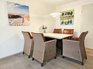 A dining area with a table and chairs, a vase with flowers, and two wall-mounted pictures. - Ok23 Oostkapelle (Oostkapelle)