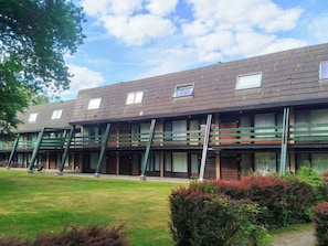A row of multi-story buildings with balconies, a grassy lawn, and a clear sky. - Ok23 Oostkapelle (Oostkapelle)