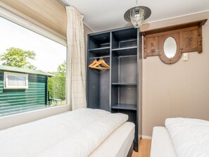 A bedroom with two beds, a wardrobe, a mirror, and a window with a view of greenery outside. - "t Ongerepte 42 (Renesse)