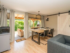 A room with a wooden dining table, chairs, a grill, and a sofa. - "t Ongerepte 42 (Renesse)