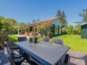 A patio with a table and chairs, a barbecue grill, and a covered seating area with outdoor furniture. - "t Ongerepte 42 (Renesse)