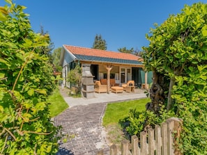 A house with a covered patio, outdoor seating, and a stone fireplace. - "t Ongerepte 42 (Renesse)